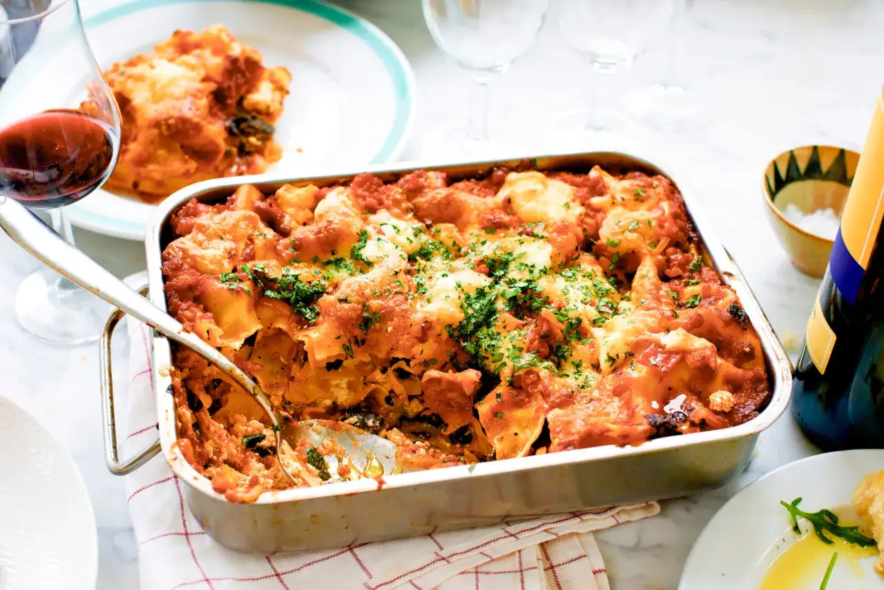En nybakad vegetarisk lasagne i formen, toppad med ost och persilja. Ett glas rödvin står bredvid.