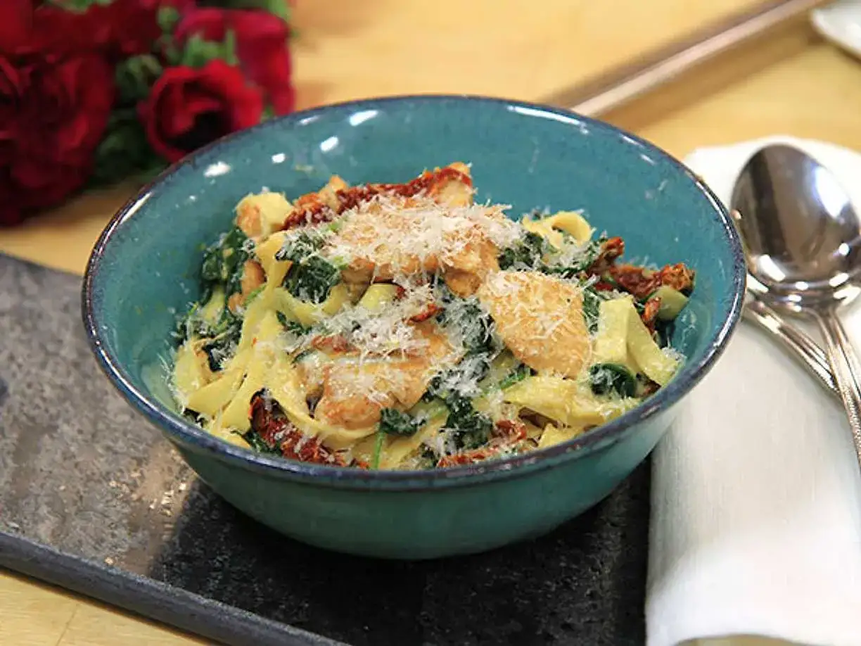 En härlig kycklingpasta med soltorkade tomater och spenat, perfekt för ett snabbt och gott kycklingpasta recept. Serveras i en blå skål med riven parmesan.