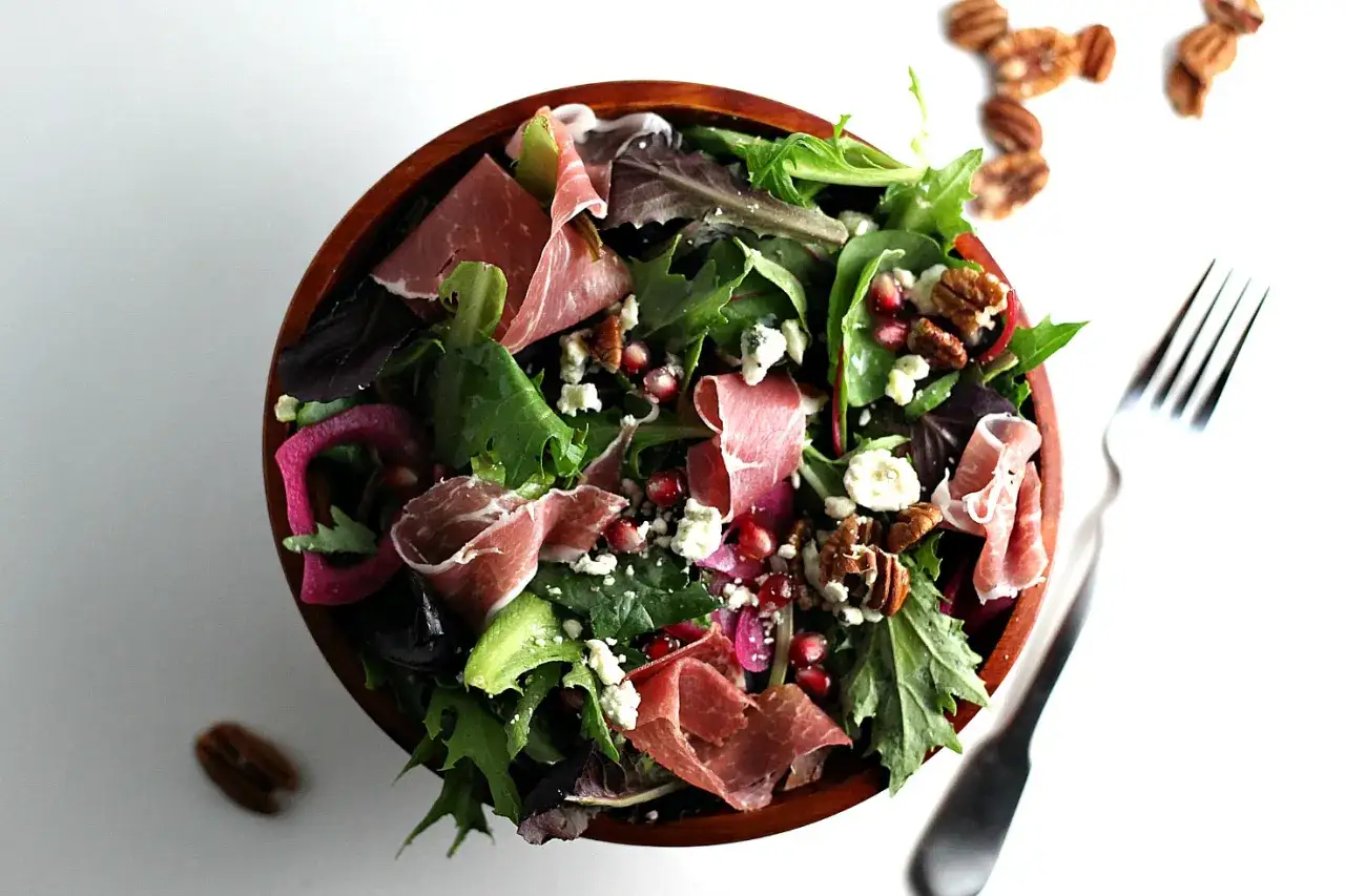 En härlig sallad med gröna blad, granatäpple, nötter, ost och tunt skivad prosciutto crudo.