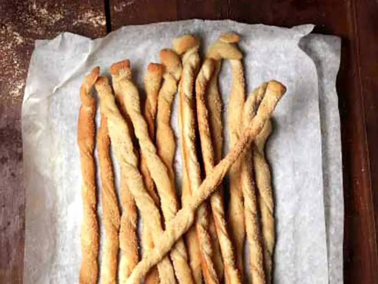 Gyllene, tvinnade grissini på bakplåtspapper. Perfekt för ett enkelt grissini recept.