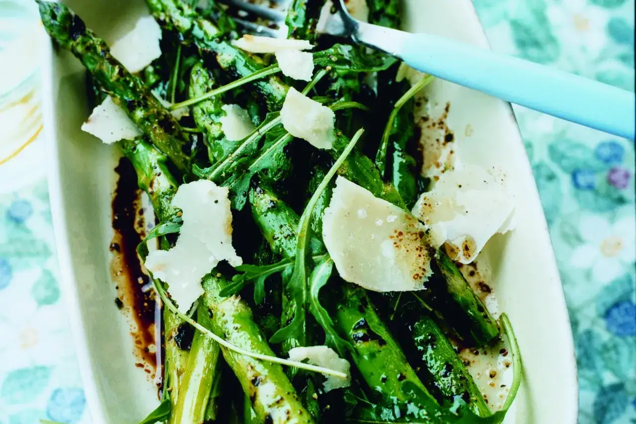 Grillad sparris med parmesan och ruccola, serverad i en vit skål med en ljusblå gaffel.