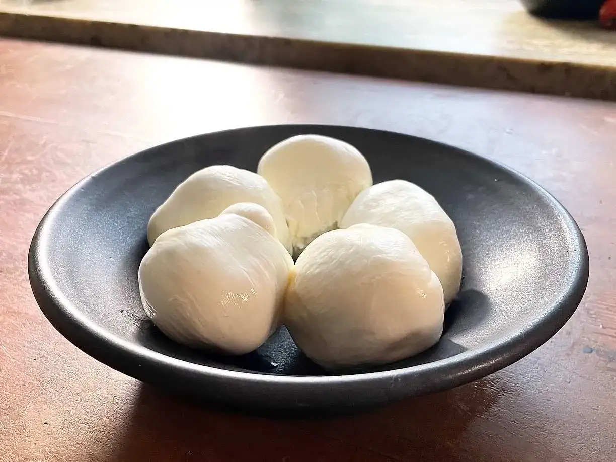 Fem små bollar färsk mozzarella i en svart skål. Perfekt för ett enkelt mozzarella recept.