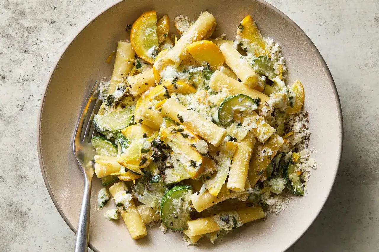 En tallrik med rigatoni pasta blandad med skivad zucchini och gul squash, toppad med riven ost och örter. En härlig zucchini pasta-rätt.