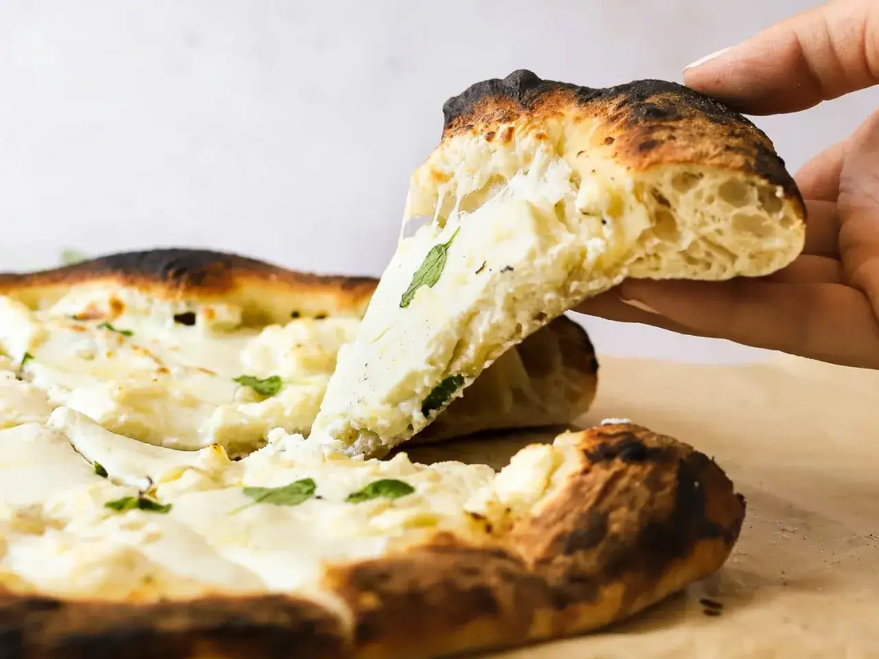 En hand lyfter en bit av en krämig pizza bianco, perfekt för ett enkelt pizza bianco recept.