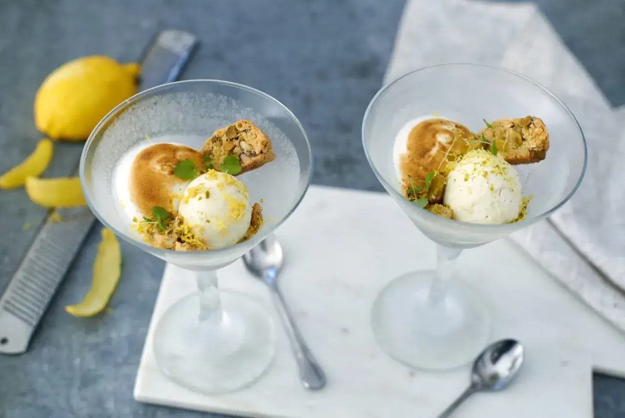 Två glas med en läcker limoncello dessert, toppad med glass, maräng och en biscotti.