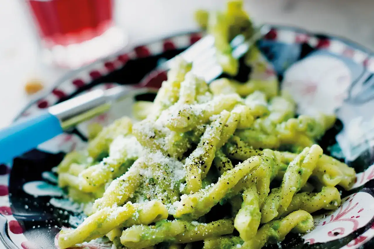En portion strozzapreti pasta med grön sås och riven ost, redo att avnjutas med en gaffel.