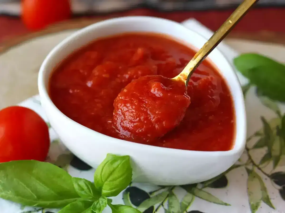 En sked fylld med hemlagad tomatsås, perfekt för pasta italiano. Tomater och basilika i närheten.