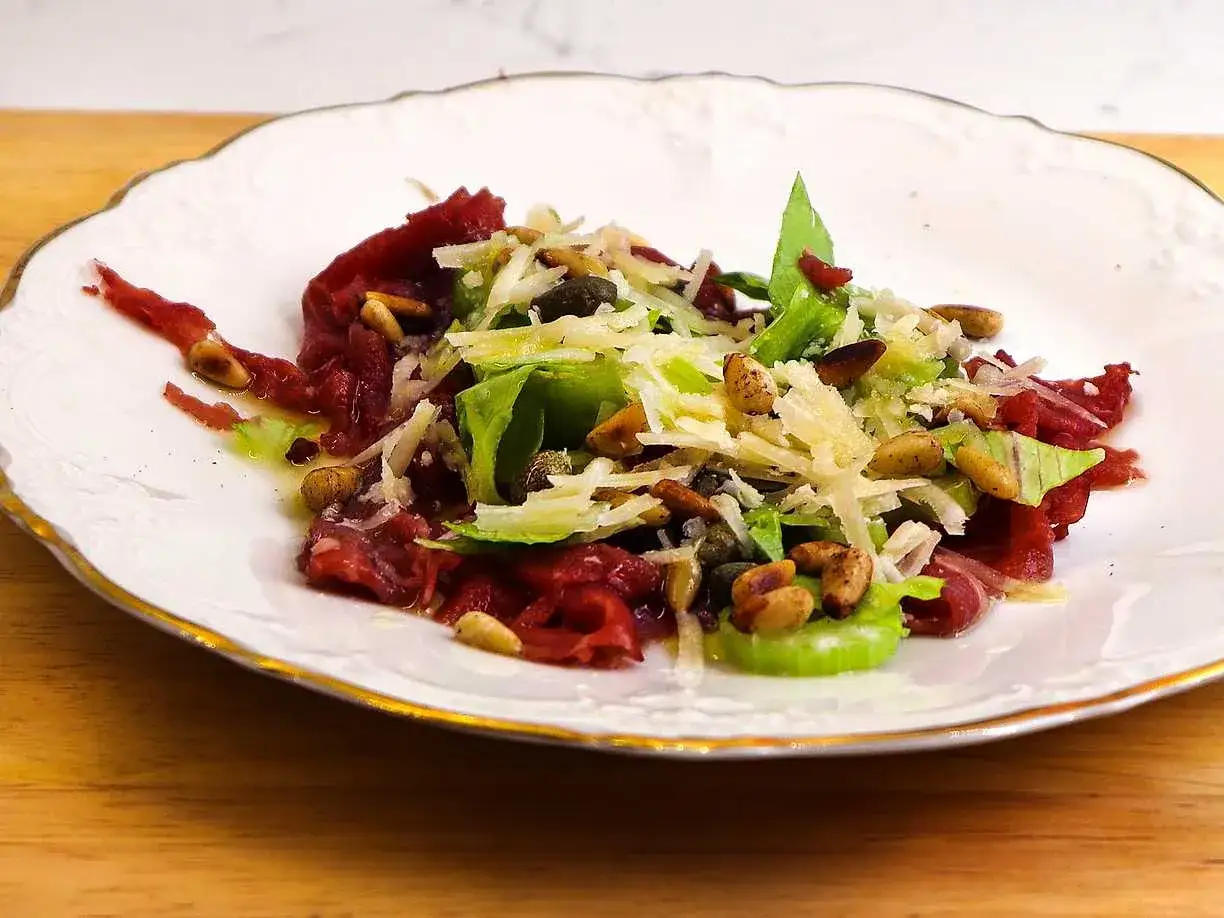 En elegant carpaccio med tunt skivad oxfilé, hyvlad parmesan, kapris, pinjenötter och en fräsch sallad. Ett perfekt carpaccio recept för en lyxig förrätt.