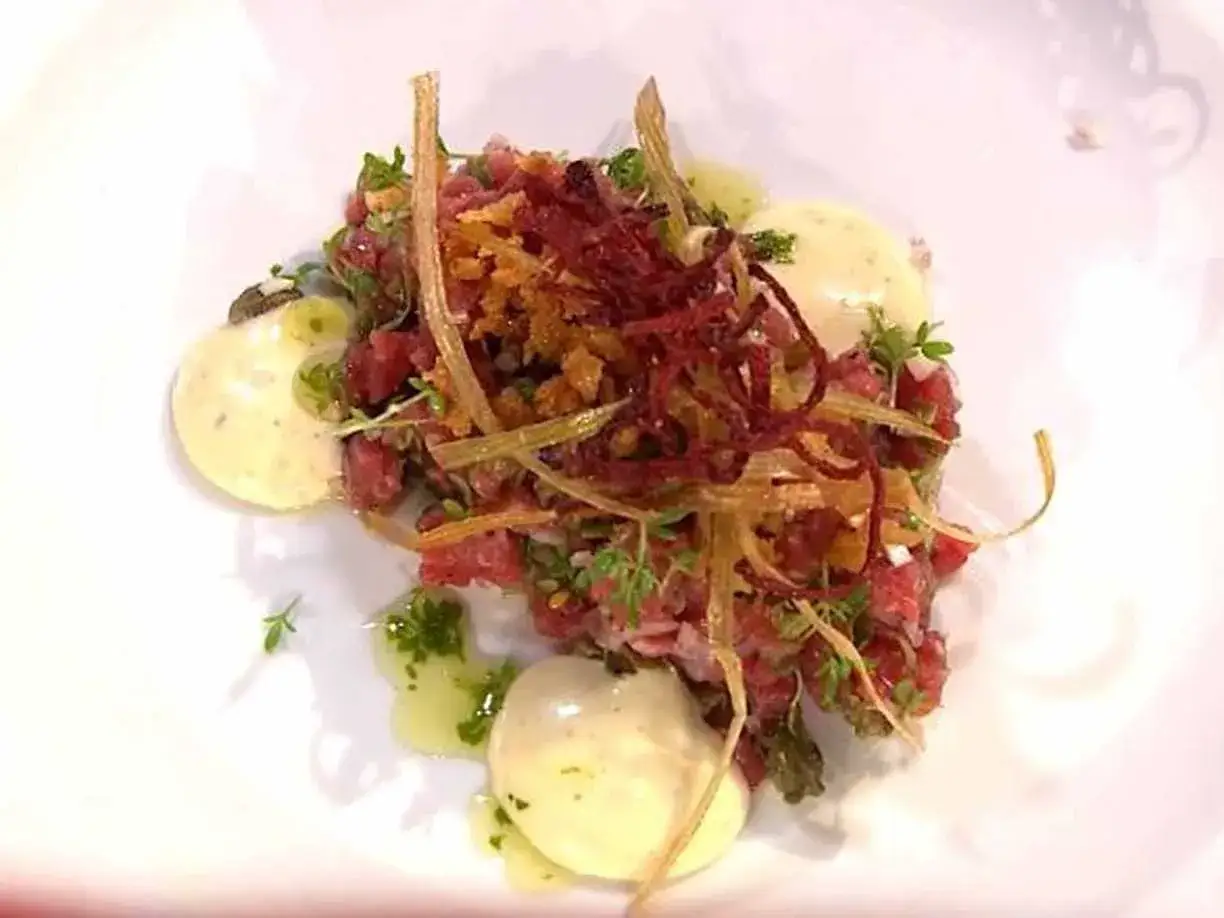 En konstnärlig tallrik med carne cruda, toppad med krispiga rotfrukter och örter, serverad med krämiga äggulor.