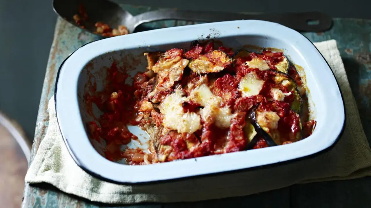 En blå ugnsform med en härlig melanzane alla parmigiana, täckt med tomatsås och smält ost. En sked med rester ligger bredvid.
