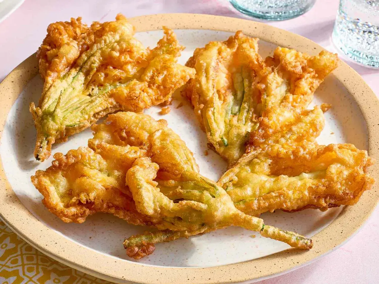 Friterad zucchiniblomma, gyllene och krispiga, ligger p&aring; en tallrik. En delikatess som sm&auml;lter i munnen.