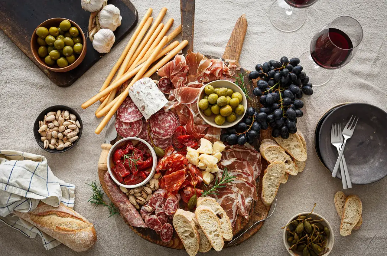 En generös charkbricka med salami napoli, prosciutto, oliver, vindruvor, bröd och nötter.