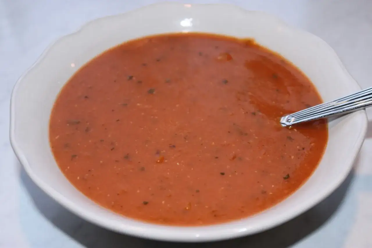 En skål med värmande linssoppa, perfekt för ett enkelt linssoppa recept. En sked vilar i den mustiga, röda soppan.