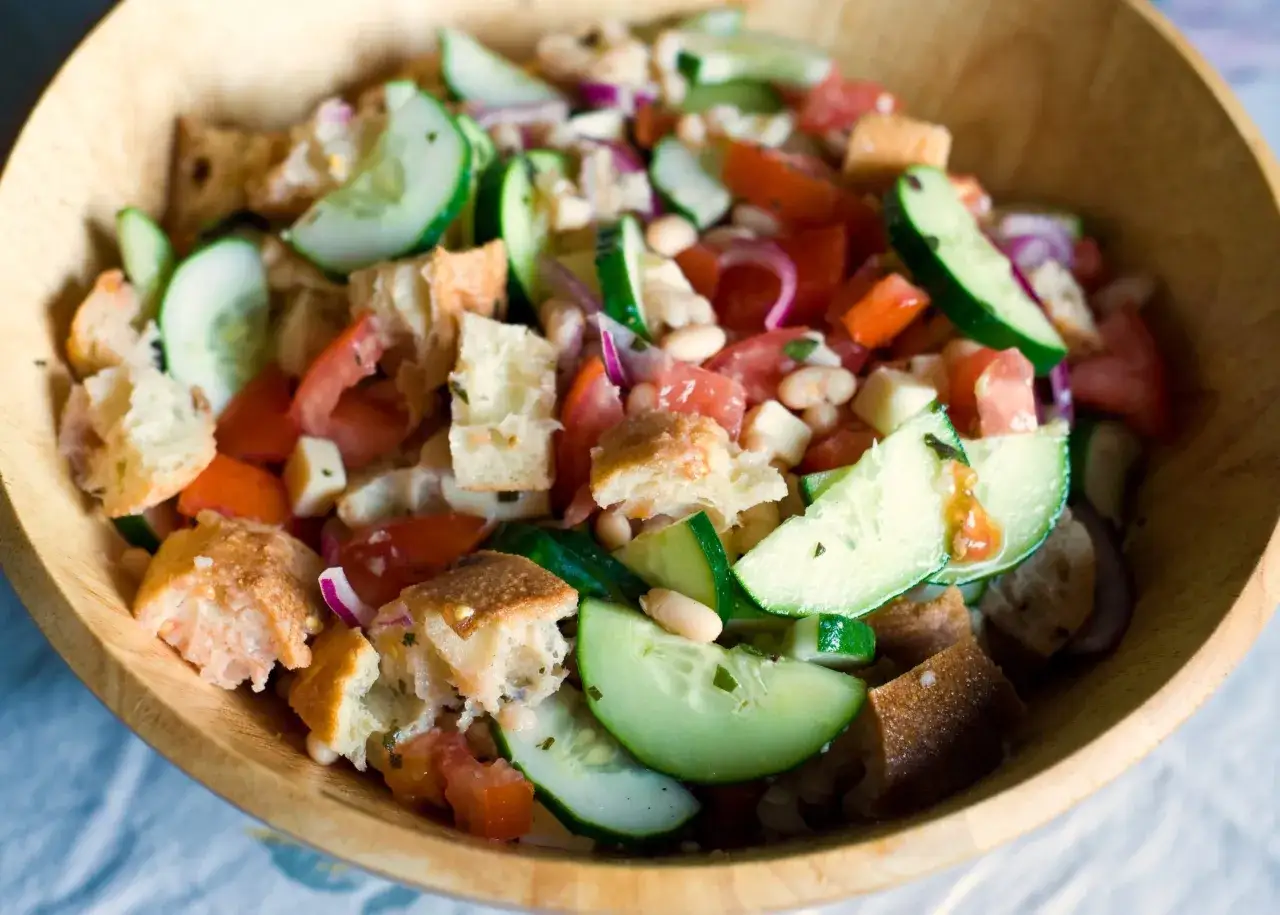 En härlig panzanella med brödkrutonger, tomat, gurka och bönor i en träskål. Perfekt för ett lätt sommarmål.