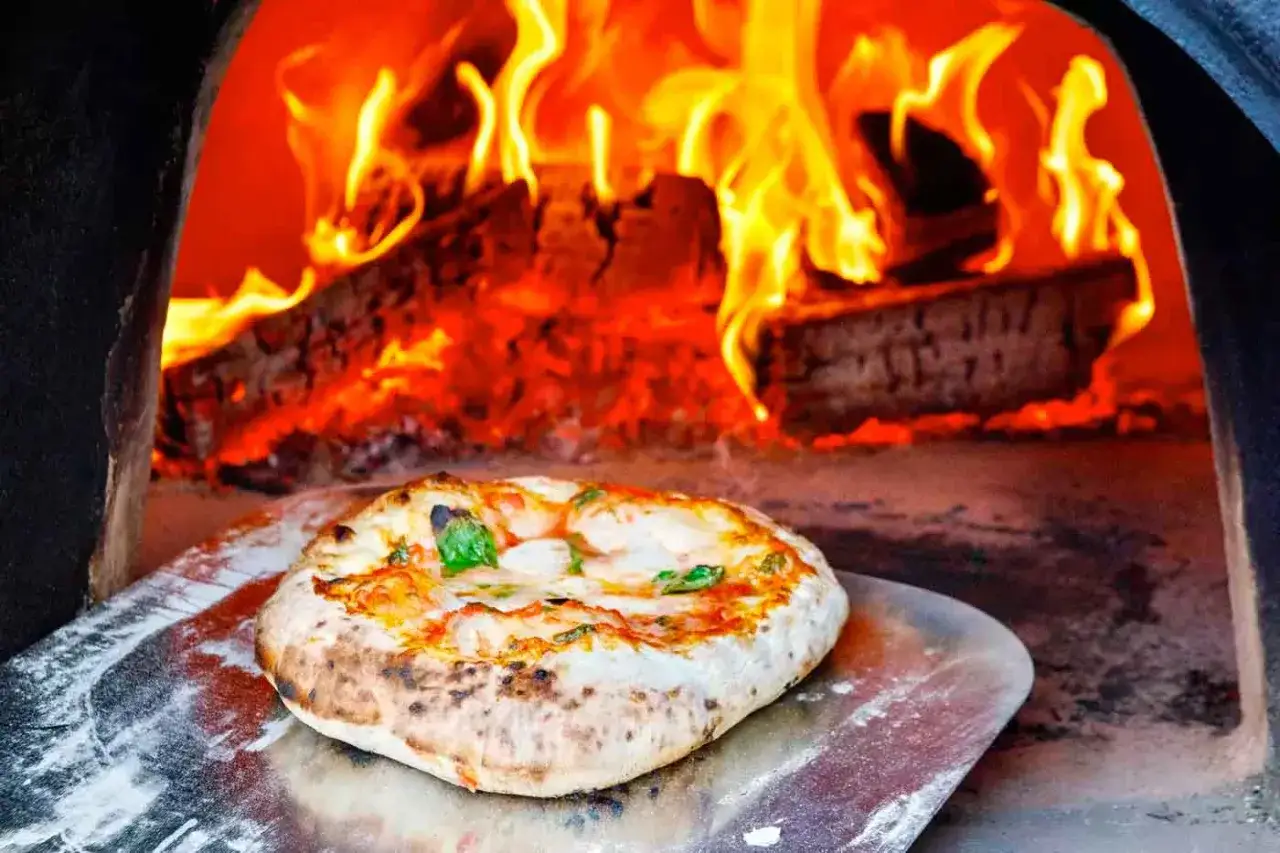 En perfekt neapel pizza med bubbliga kanter och färsk basilika tas ur en vedeldad ugn med flammande eld.