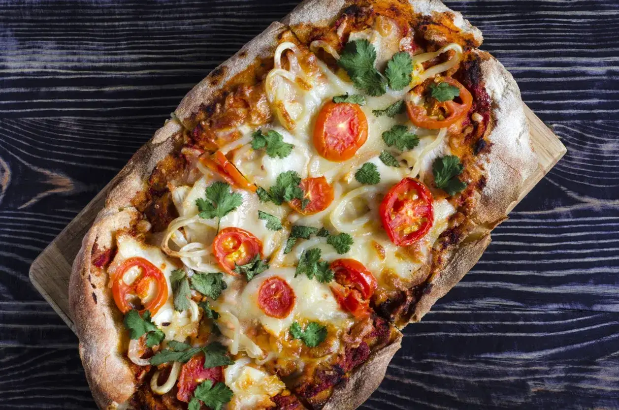 En avlång, nybakad italien pizza med tomater, lök och färsk koriander på en mörk träbakgrund.