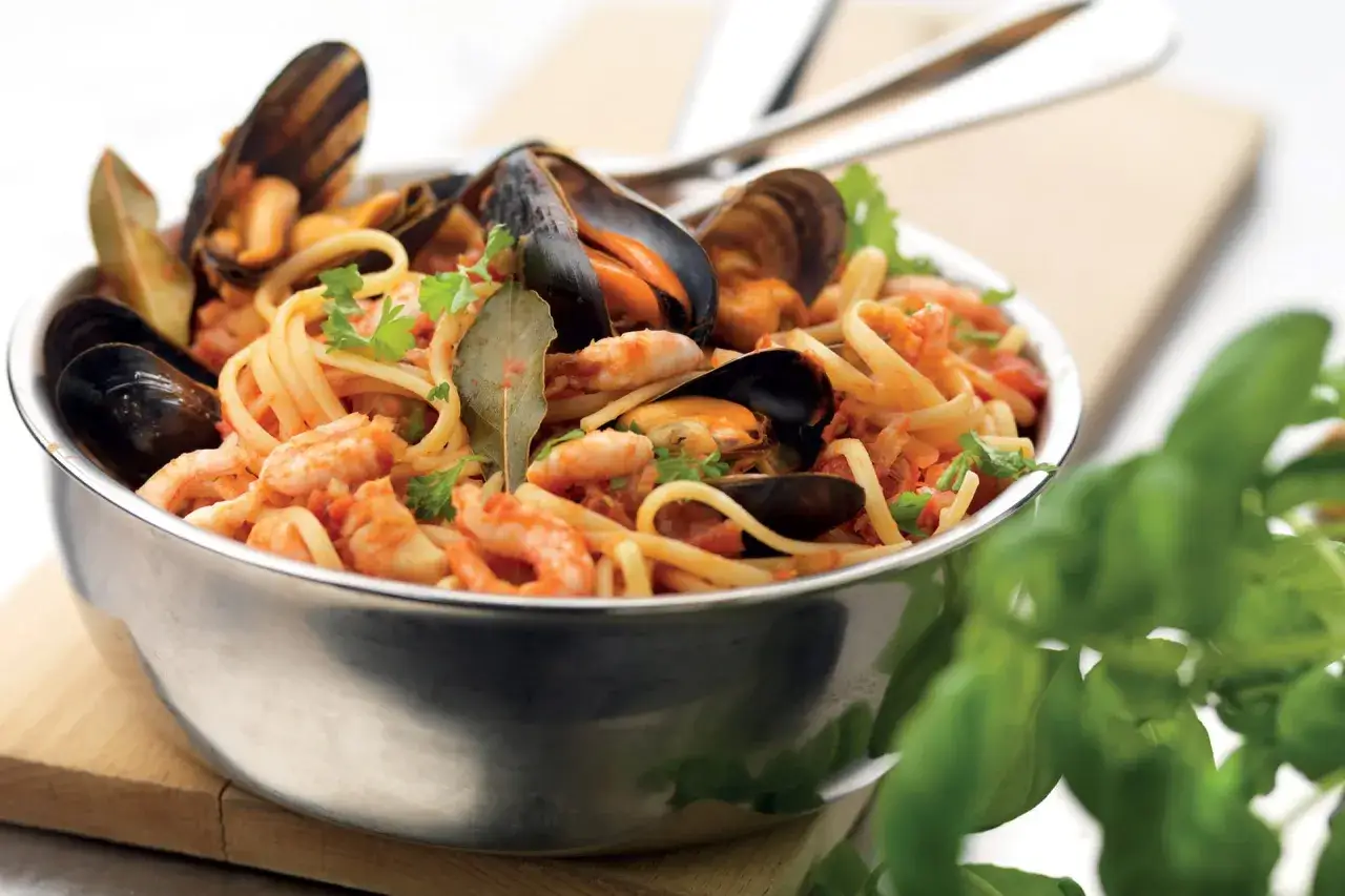 En skål med frutti di mare pasta, fylld med musslor, räkor och linguine i en tomatsås, garnerad med persilja och lagerblad.