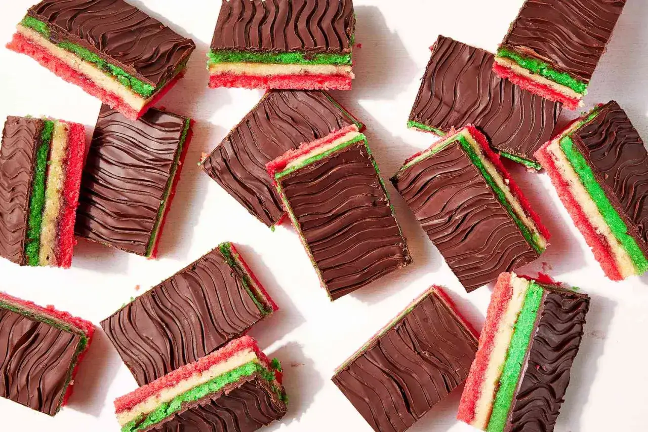 Flera rektangulära bitar av en italiensk dessert med lager av rött, vitt och grönt kex, täckta med mörk choklad med vågmönster.