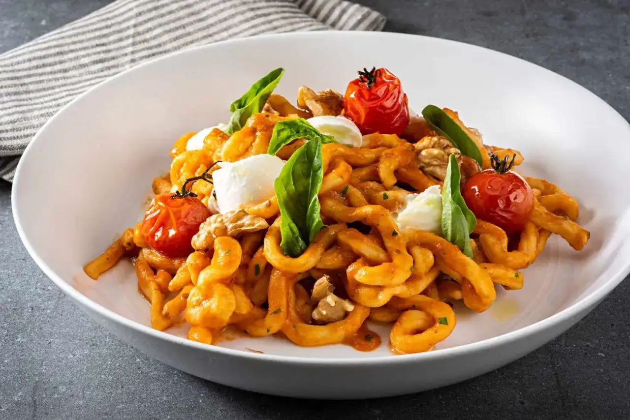 En skål med krökt durumvete pasta med tomater, nötter, mozzarella och basilika.