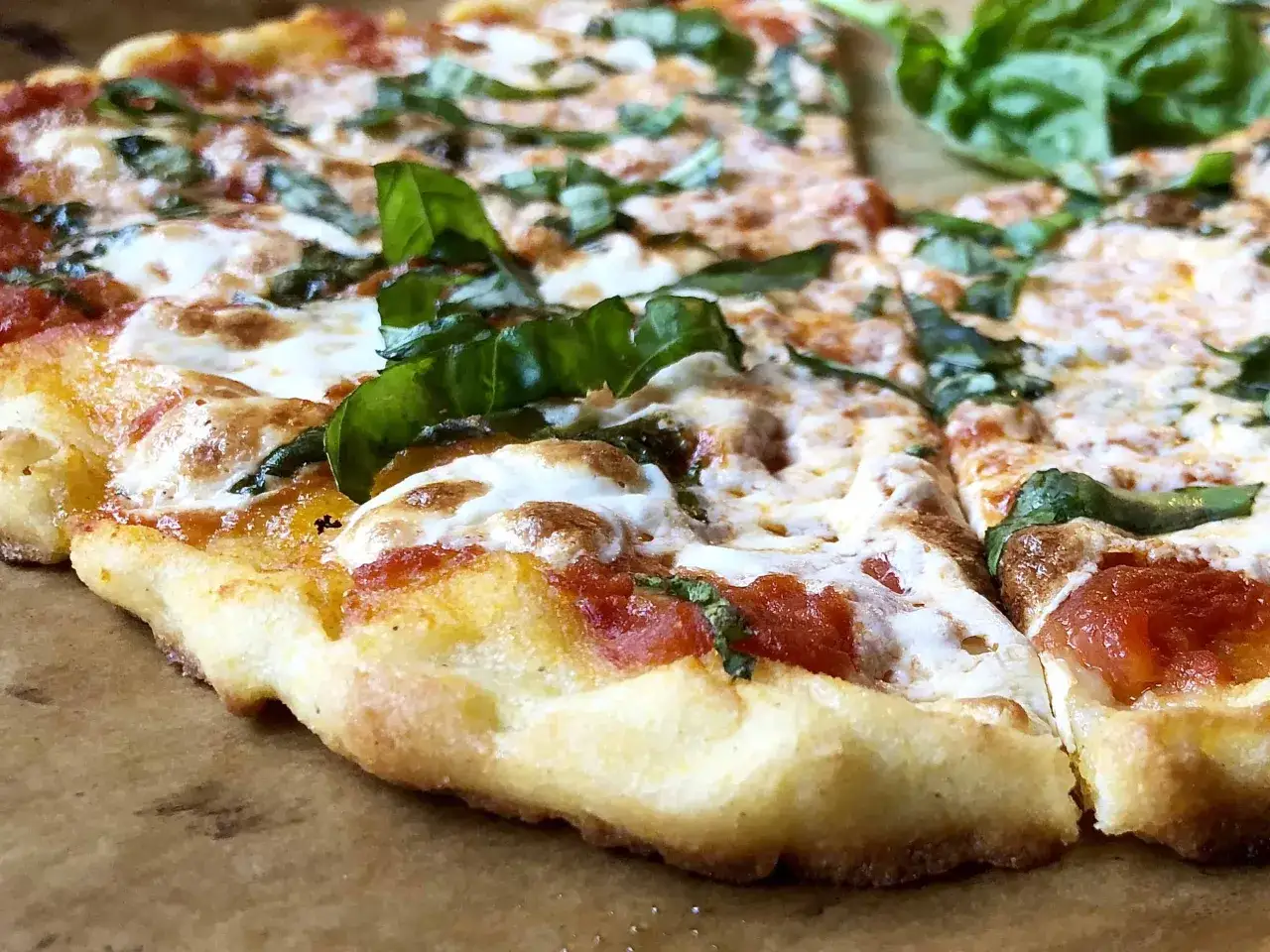 En närbild av en glutenfri pizza med smält ost, tomatsås och färsk basilika. Ett perfekt glutenfri pizzadeg recept!