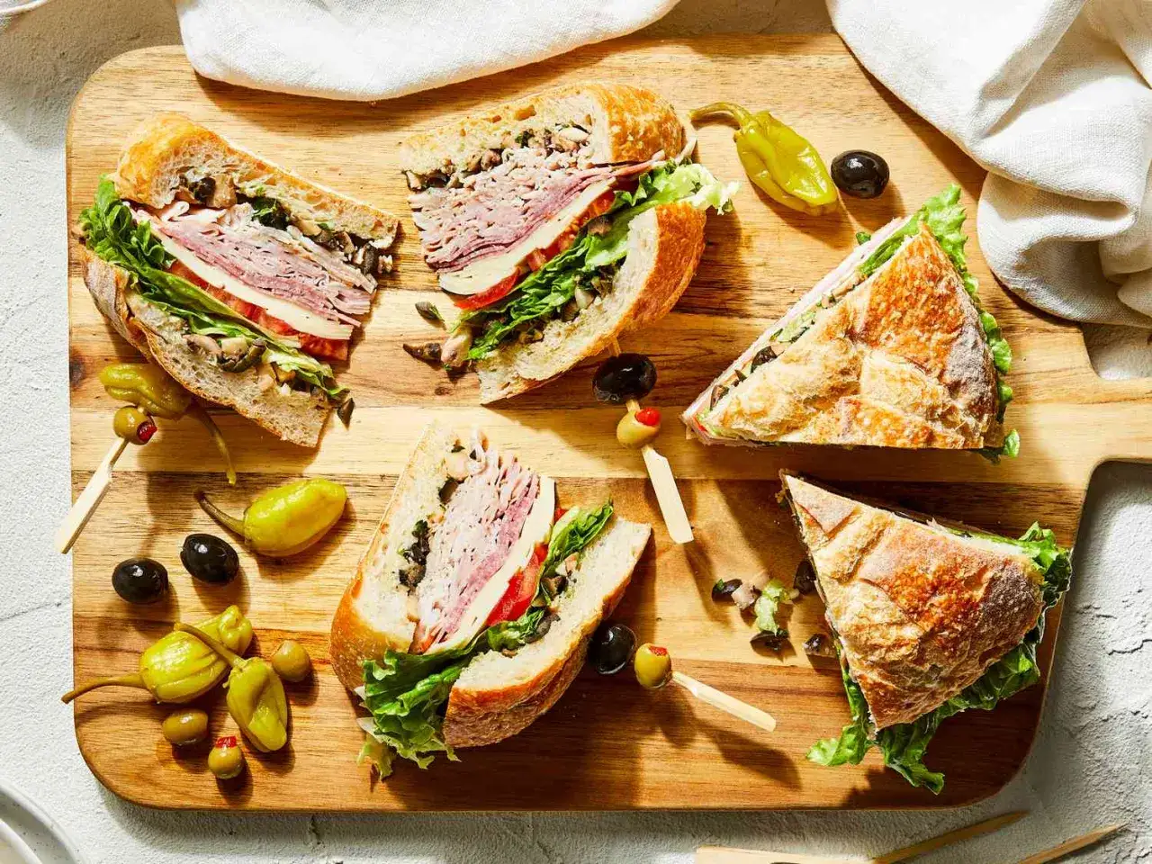 En härlig italiensk macka, uppdelad i bitar, med kött, ost, sallad och oliver på en träskärbräda.