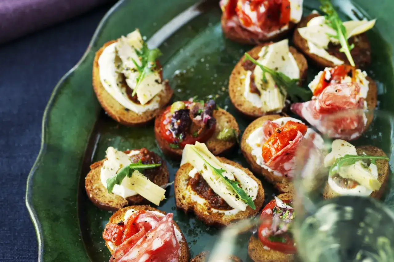 En grön tallrik med olika crostini-toppningar: salami, tomat, ost och ruccola.
