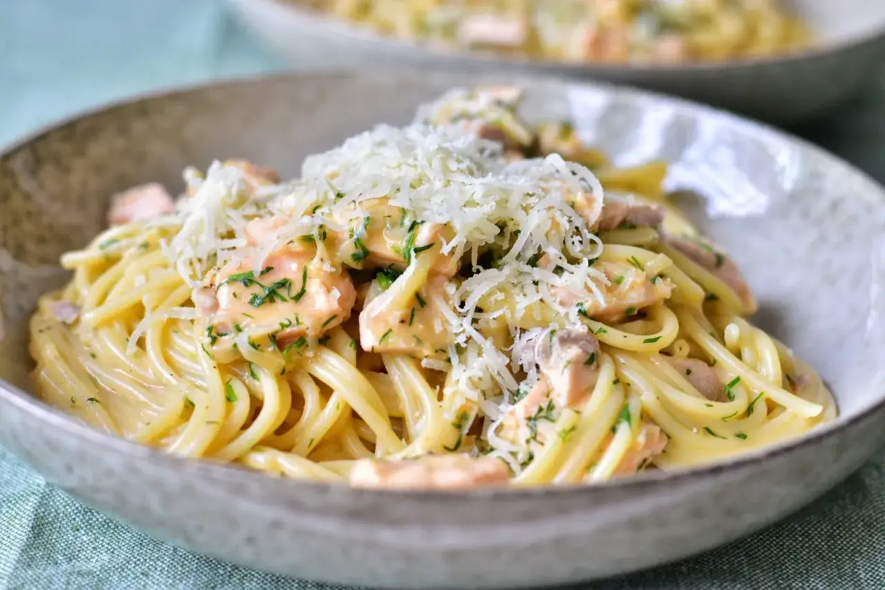 En närbild av en skål med krämig laxpasta, toppad med riven ost och färsk persilja. Ett perfekt laxpasta recept för en snabb middag.
