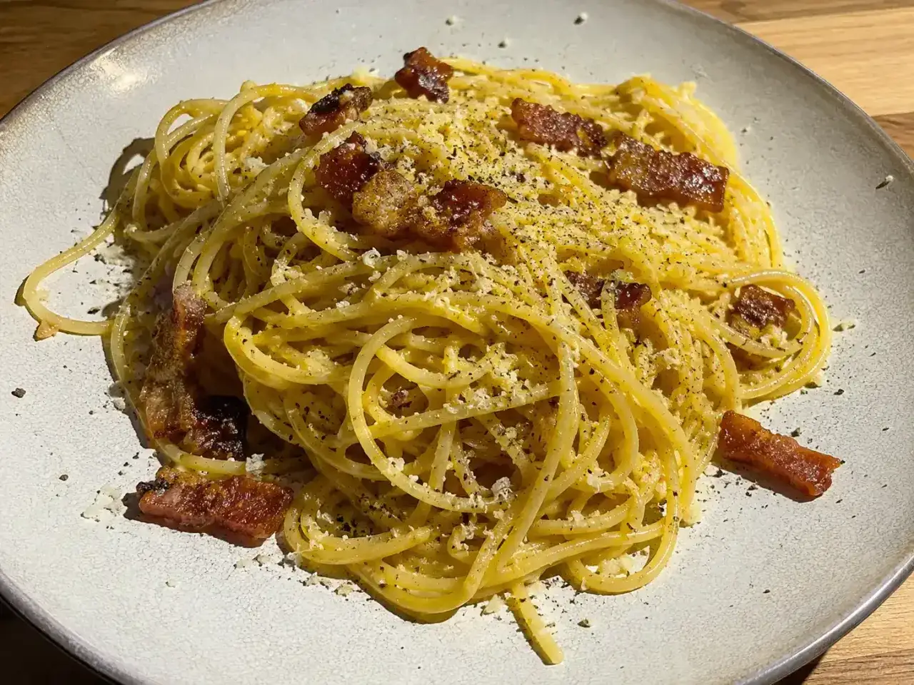En portion klassisk carbonara med spaghetti, toppad med stekt sidfläsk och riven ost.