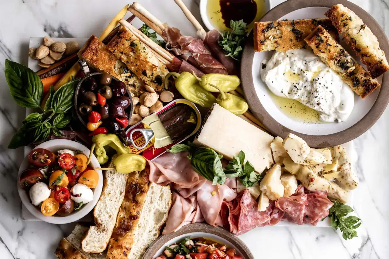 En generös italiensk charkbricka med oliver, tomater, burrata, salami, prosciutto, kronärtskocka, bröd och sardiner.