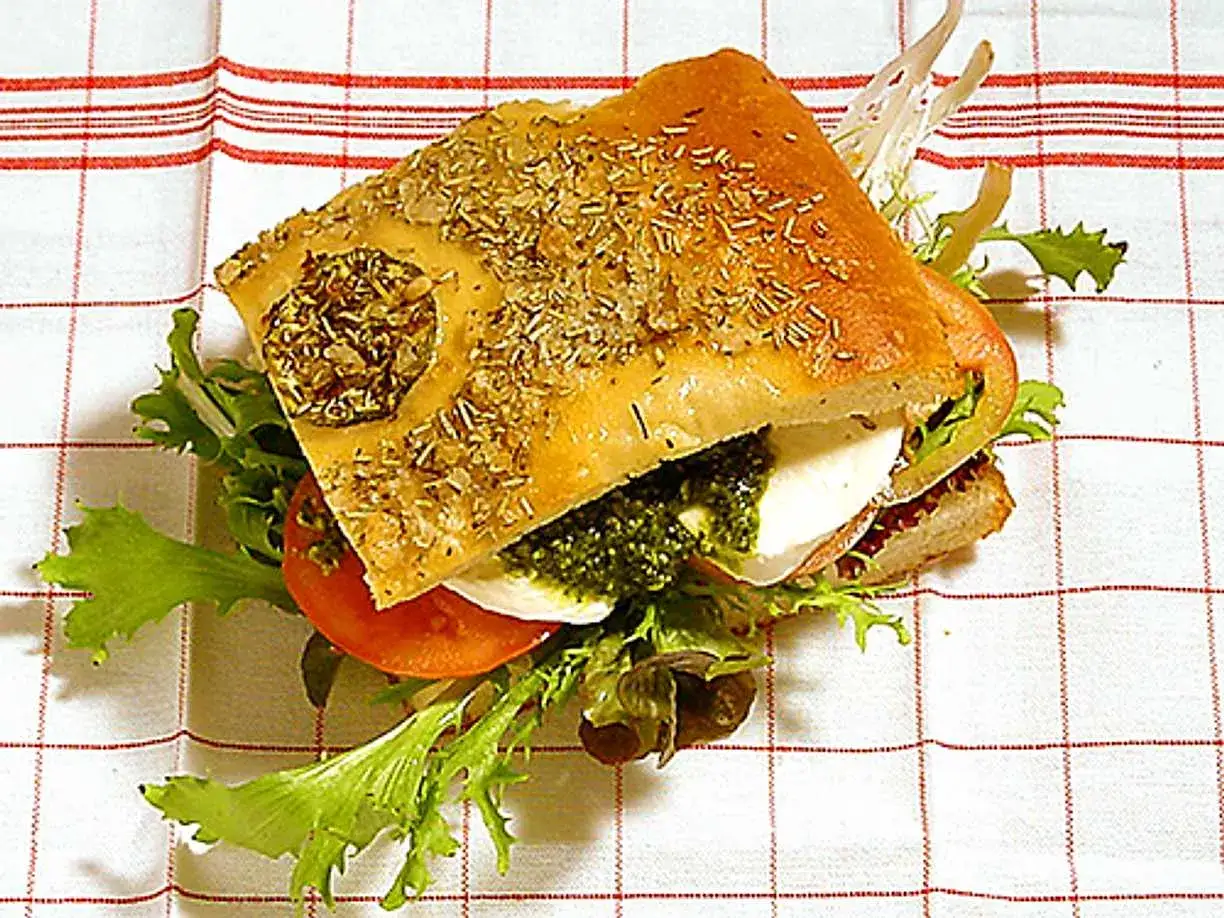 En läcker pesto macka med focaccia, mozzarella, tomat och grönsaker på en rutig duk.