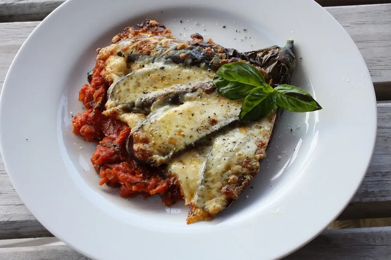 En tallrik med vegetarisk italiensk mat, aubergine gratinerad med ost och tomatsås, toppad med färsk basilika.