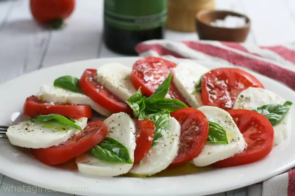 En vacker napolitansk sallad med skivade tomater, mozzarella och färsk basilika, ringlad med olivolja och peppar.