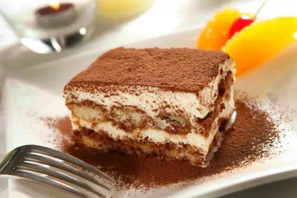 En bit krämig italiensk dessert, tiramisu, pudrad med kakao. Garnerad med apelsin och körsbär.