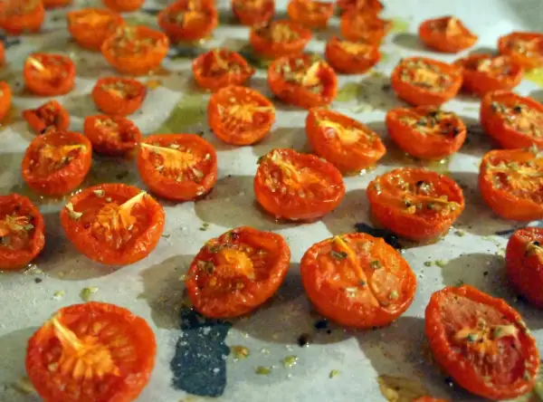 Halverade, semitorkade tomater ligger utspridda på en bakplåt. De ser saftiga och smakrika ut, redo att användas i matlagning.