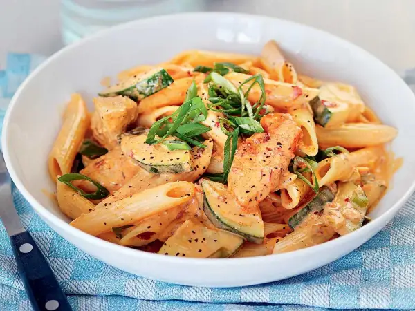 Enkel pasta med kyckling och zucchini i krämig tomatsås, toppad med salladslök.