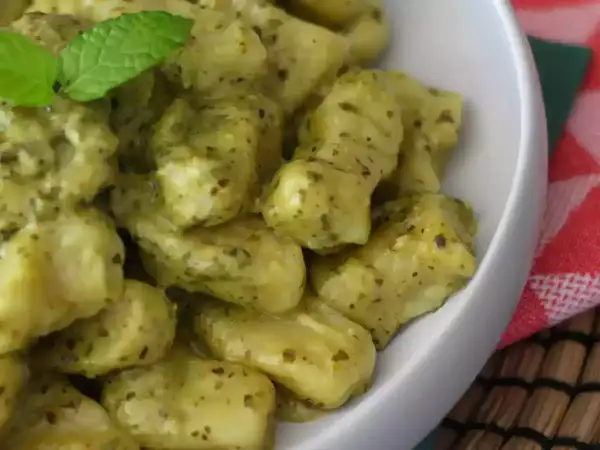 En skål med krämiga gnocchi pasta med pesto och en myntakvist.