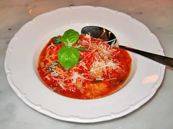 En portion pappa al pomodoro, en mustig tomatsoppa med bröd, toppad med basilika och parmesan. En sked ligger i skålen.
