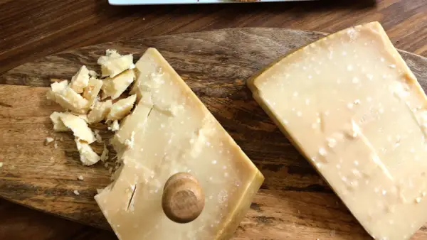 Två bitar Grana Padano parmesanost på en träskärbräda. En bit är uppbruten i mindre bitar.