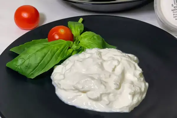 En krämig hög av stracciatella ost på en svart tallrik, dekorerad med färsk basilika och körsbärstomater.